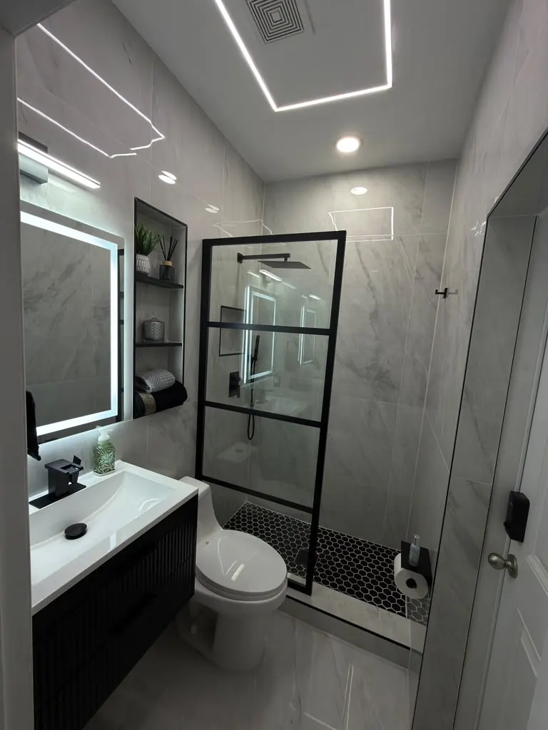 Modern bathroom in grey marble-look porcelain with a black glass panel and LED mirror